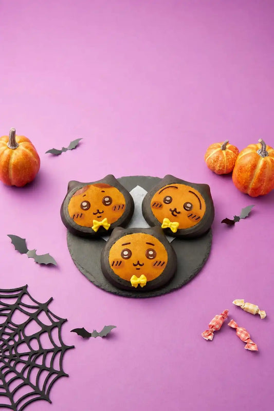 Three Chiikawa Bakery black-cat Halloween breads with orange faces and yellow bow ties on a slate plate